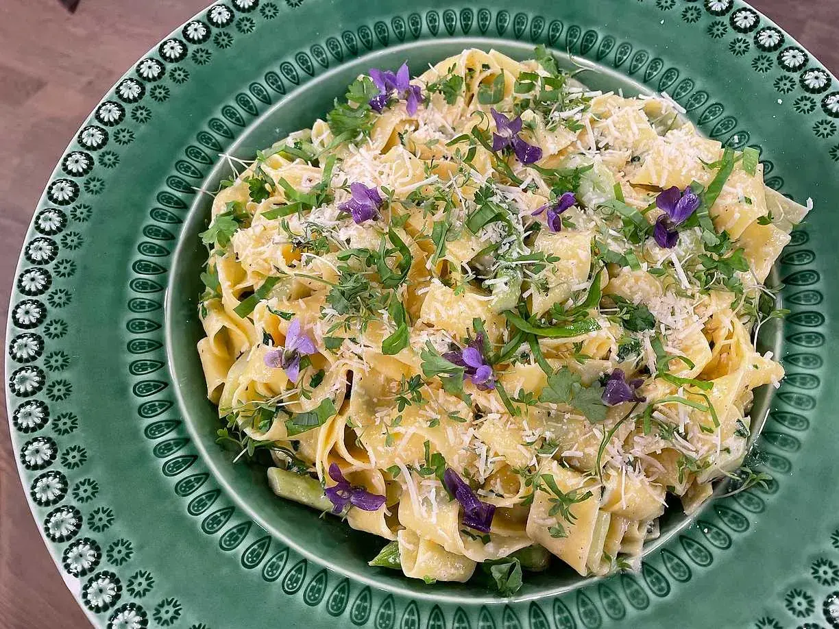 Krämig sparris pasta med färska örter och violblommor, toppad med riven parmesan. En härlig vårrätt!
