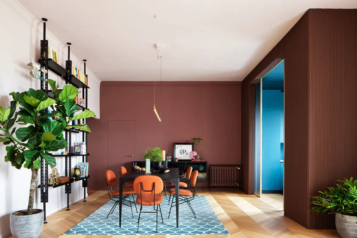 Un soggiorno moderno con pareti color mattone, sedie arancioni vivaci e un tappeto blu. Un esempio di come abbinare il color mattone con tocchi audaci.