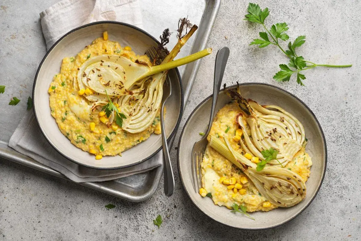 Deux bols de polenta crémeuse avec du fenouil rôti, du maïs et du persil.