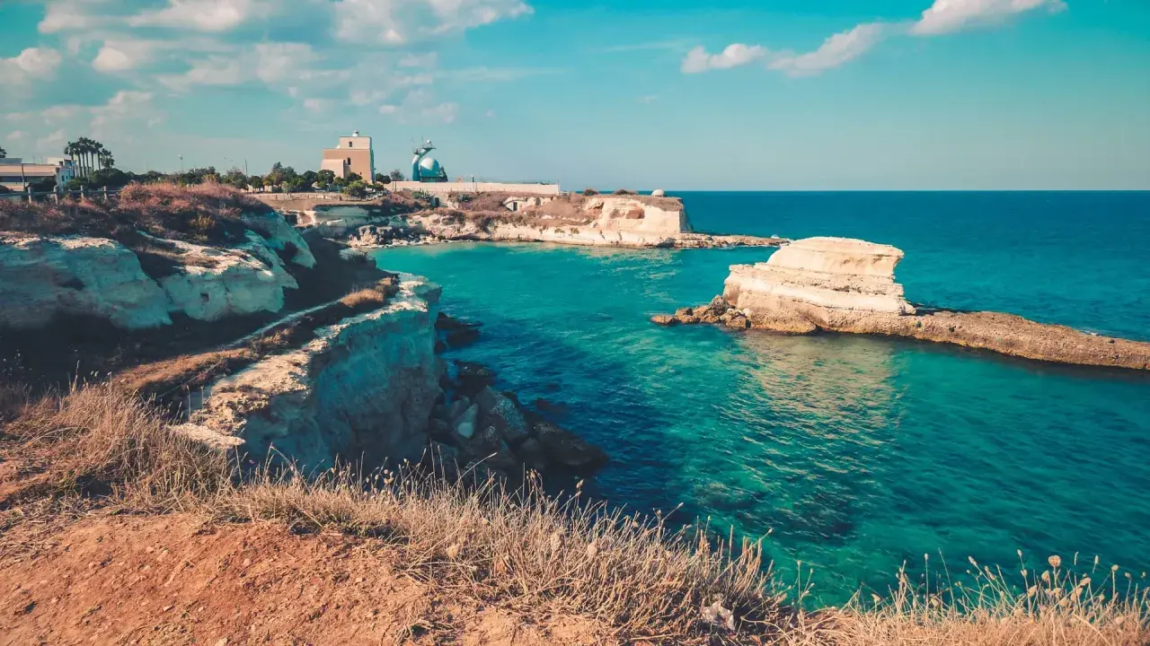 Côte rocheuse italienne aux eaux turquoise, avec des falaises et des formations rocheuses dans la mer.