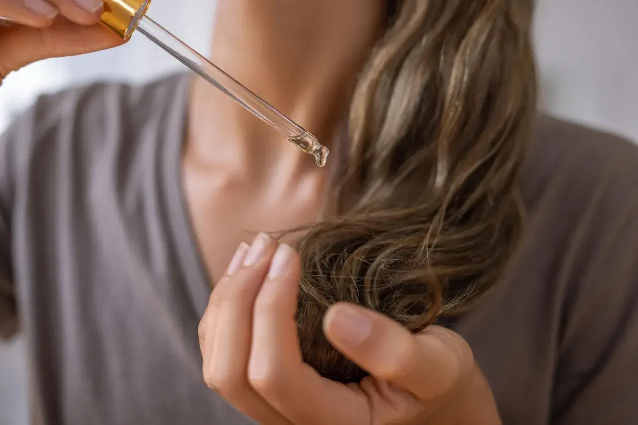 Una gota de aceite de aguacate para el pelo cae de un gotero sobre un mechón de cabello.