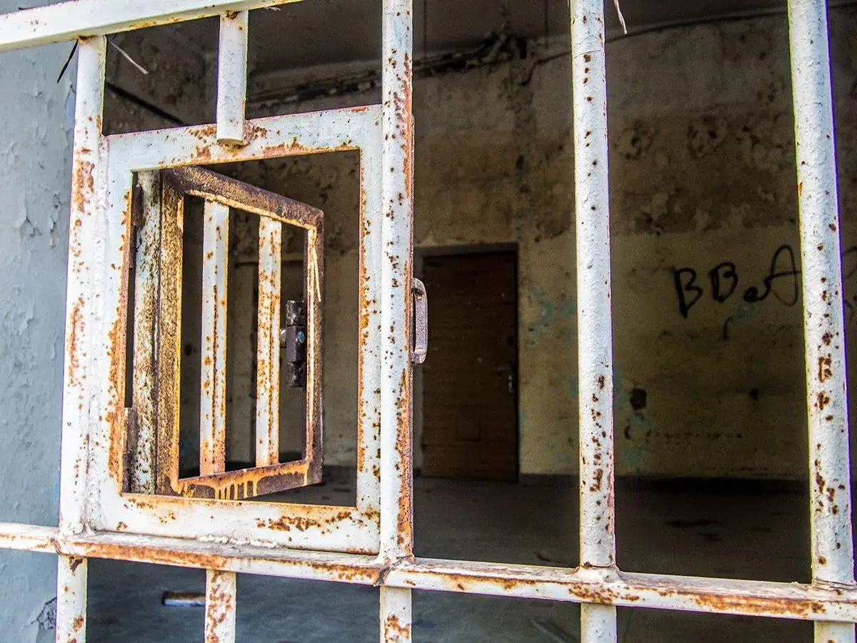 Grille rouillée d'une cellule abandonnée, porte ouverte. Un vestige de l'urbex à Laval, où le passé murmure.