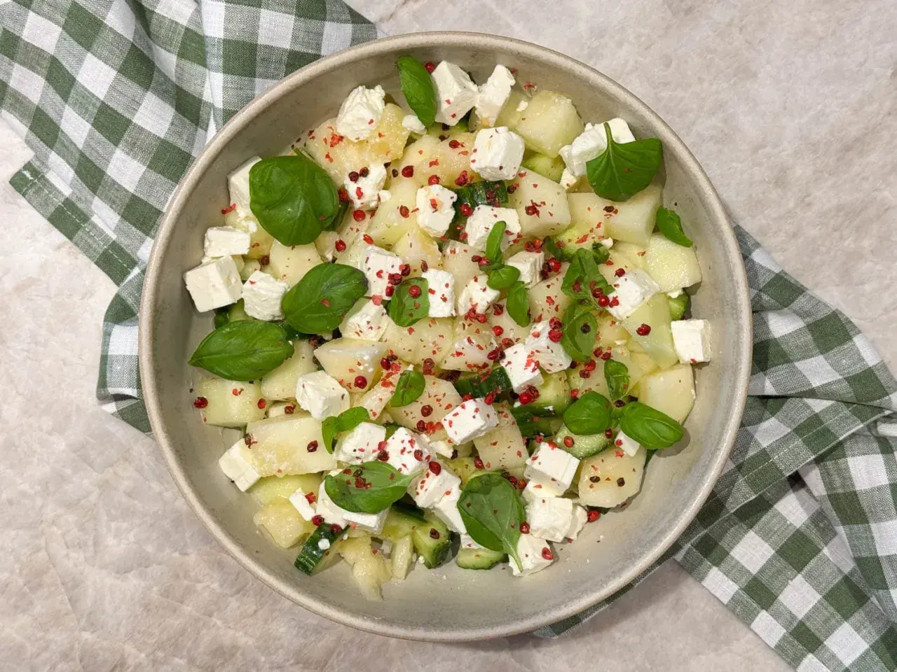 En uppfriskande melonsallad med honungsmelon, fetaost, gurka och basilika, toppad med rosa pepparkorn.