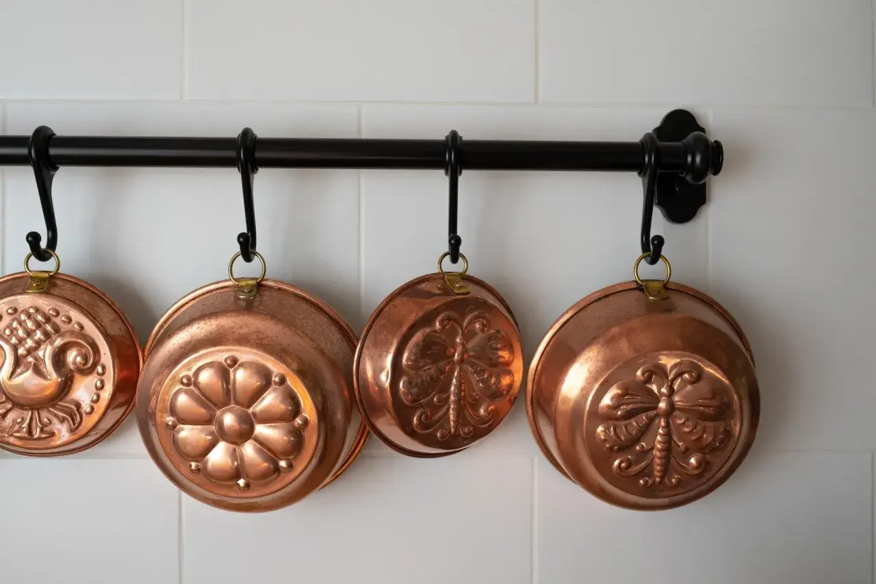 Cuencos de cobre decorados cuelgan de una barra. Aprende como limpiar cobre para que brillen así.