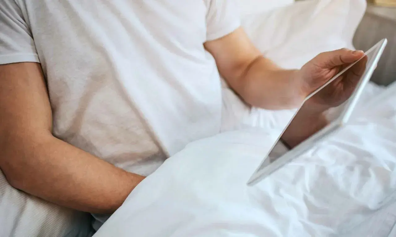 Persona in letto con tablet, forse cercando informazioni su che significa masturbare.