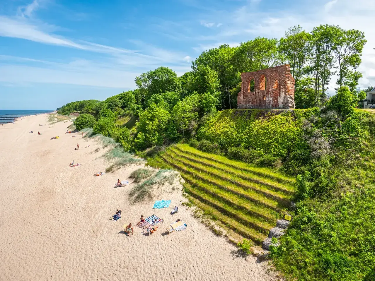 Piękny klif w Trzęsaczu z ruinami kościoła na szczycie. Piaszczysta plaża z wypoczywającymi ludźmi poniżej.