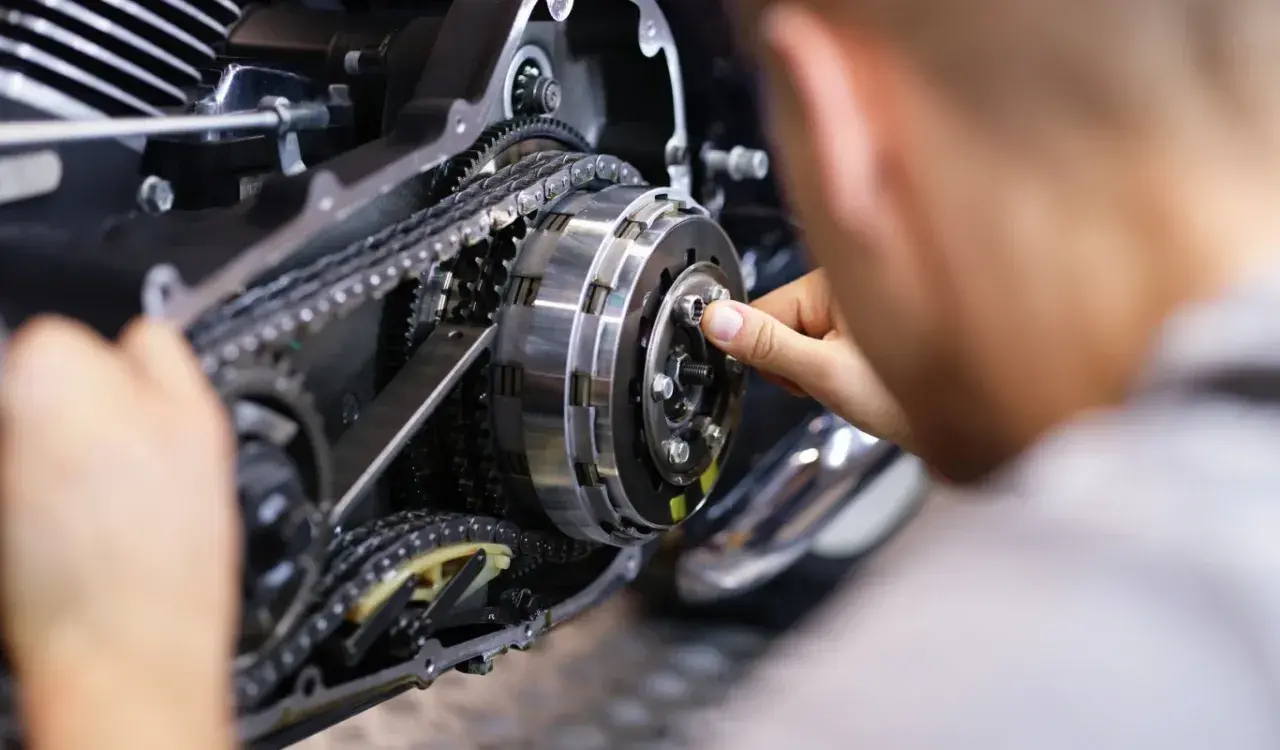 Mechanik naprawia sprzęgło motocykla, widoczny mechanizm z łańcuchem i zębatkami.