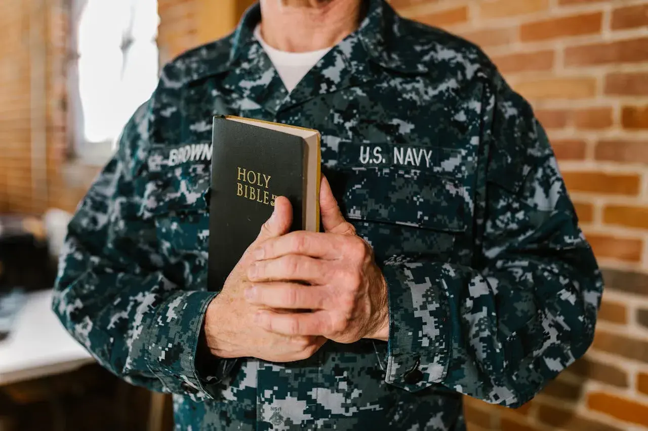 Marynarz w mundurze US Navy trzyma Biblię. W jego dłoniach spoczywa księga, niczym pieśń nad pieśniami, symbol wiary i nadziei.