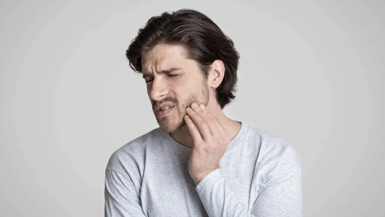 Uomo con mano sulla guancia, espressione di dolore. Potrebbe soffrire di disestesia o parestesia.