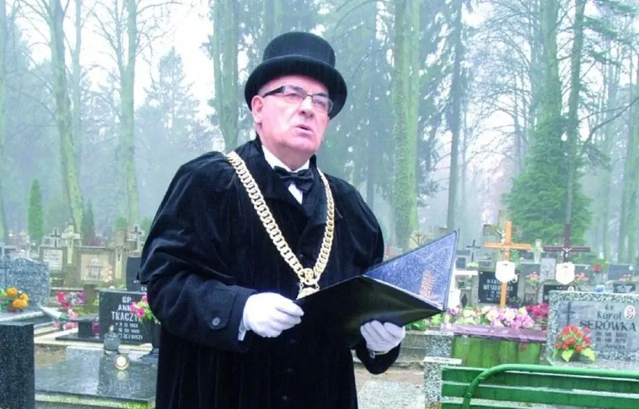 Mistrz ceremonii w czarnym stroju i z łańcuchem na szyi prowadzi pogrzeb świecki, podkreślając różnicę między nim a wyznaniowym.