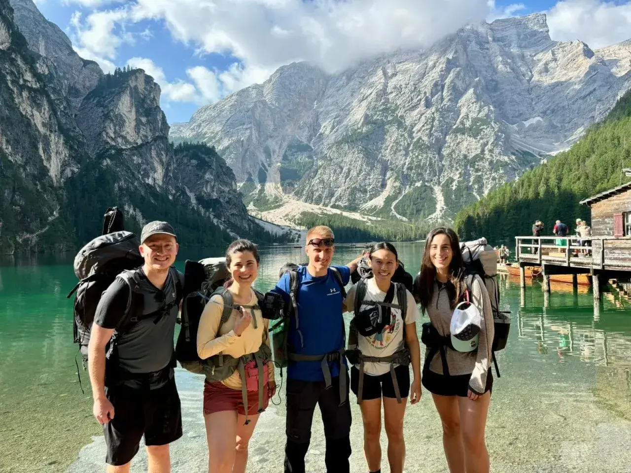Cinco excursionistas sonríen junto a un lago turquesa con imponentes montañas de **Alta Ribagorza** al fondo.