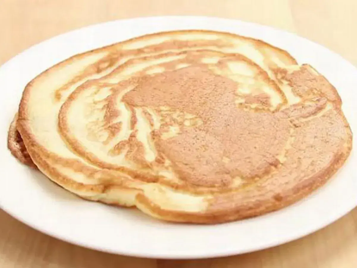 Ein goldbrauner Pfannkuchen ohne Ei auf einem weißen Teller, perfekt für ein leichtes Frühstück.