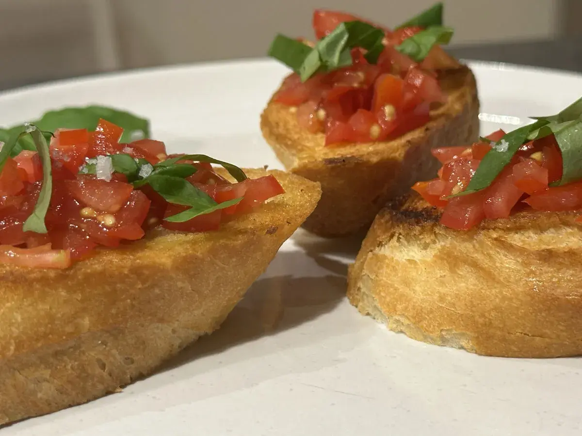 Drei Bruschetta-Scheiben mit Tomaten und Basilikum auf einem Teller.