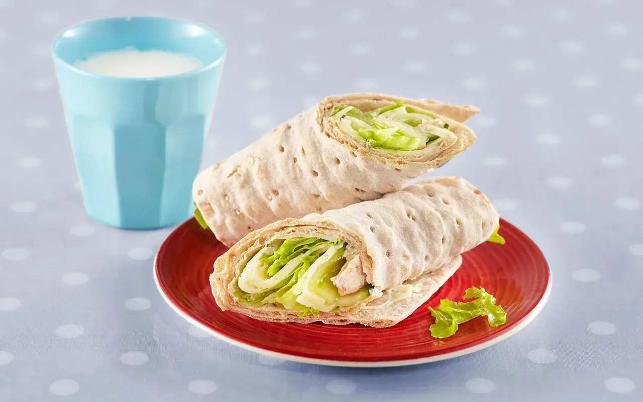 Två saftiga tonfisk wraps med krispig sallad på en röd tallrik, bredvid ett glas mjölk.