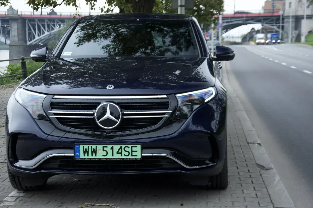 Ciemnoniebieski Mercedes EQC z tablicą rejestracyjną WW 514SE zaparkowany przy ulicy, w tle most.