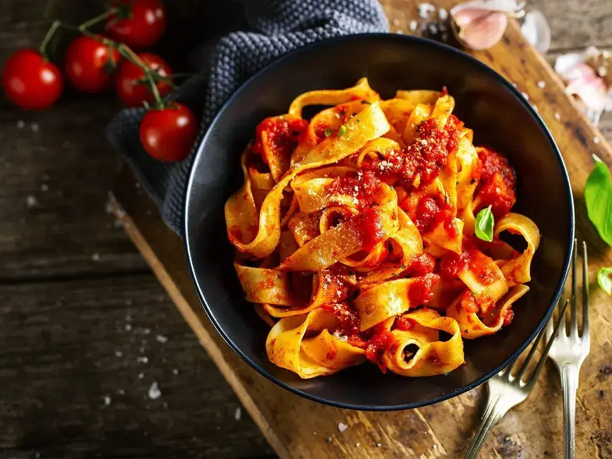 Pappardelle z sosem pomidorowym, świeże pomidory i bazylia. Pyszne dania z pomidorów na drewnianym blacie.