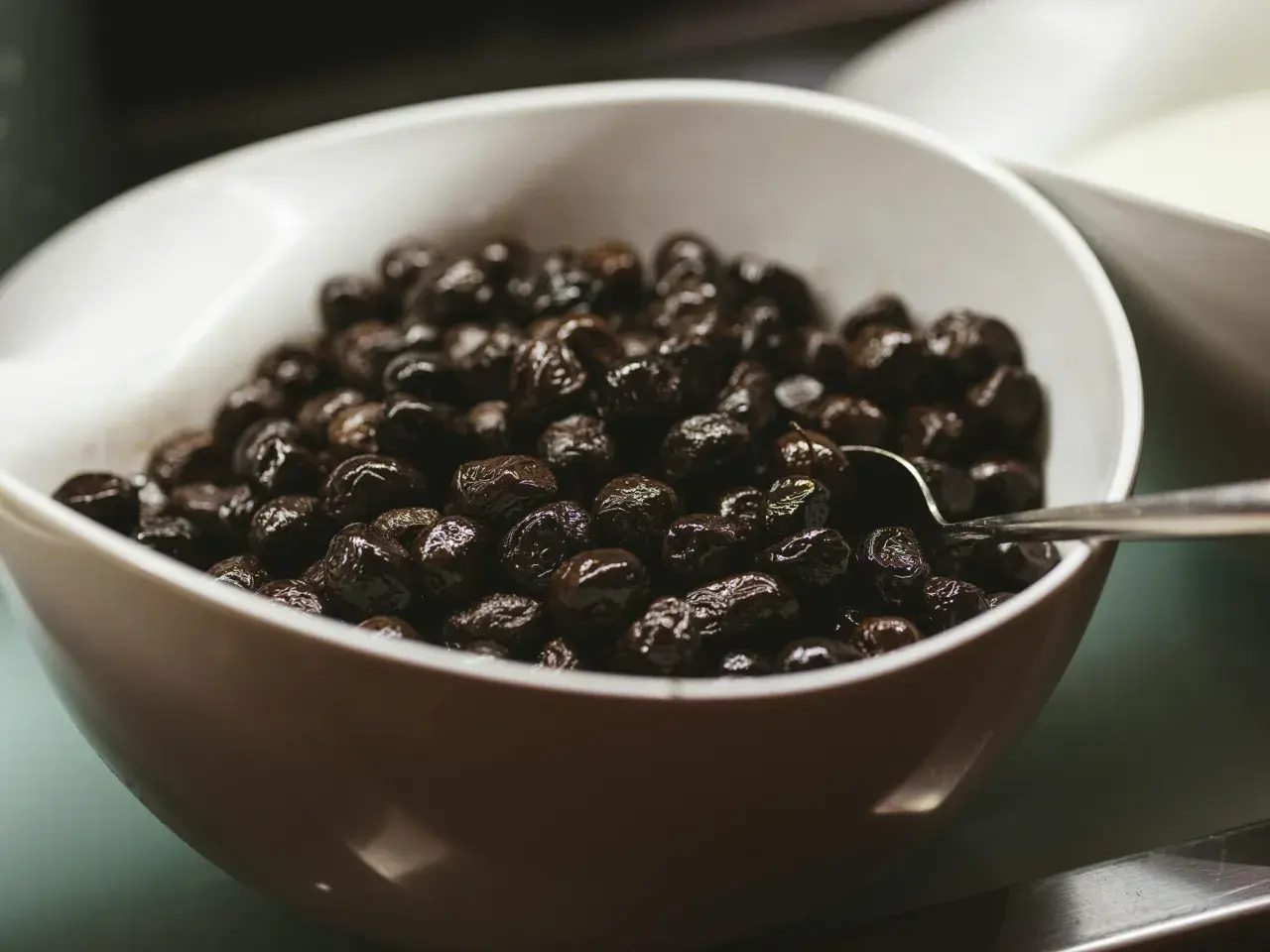 Un cuenco blanco lleno de aceitunas negras brillantes, perfecto para tus recetas con aceitunas negras.