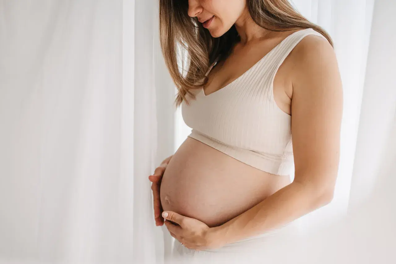 Gravid kvinna med händer på magen, mjukt ljus. Hon kanske använder bio oil gravid för att ta hand om sin hud.