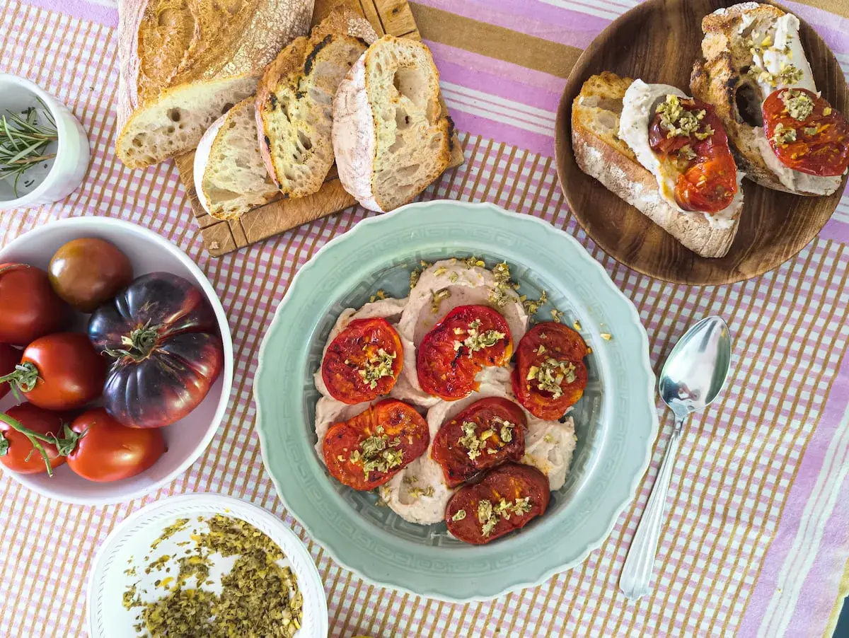 Tomates italianos asados sobre una crema suave, acompañados de pan rústico y tomates frescos.