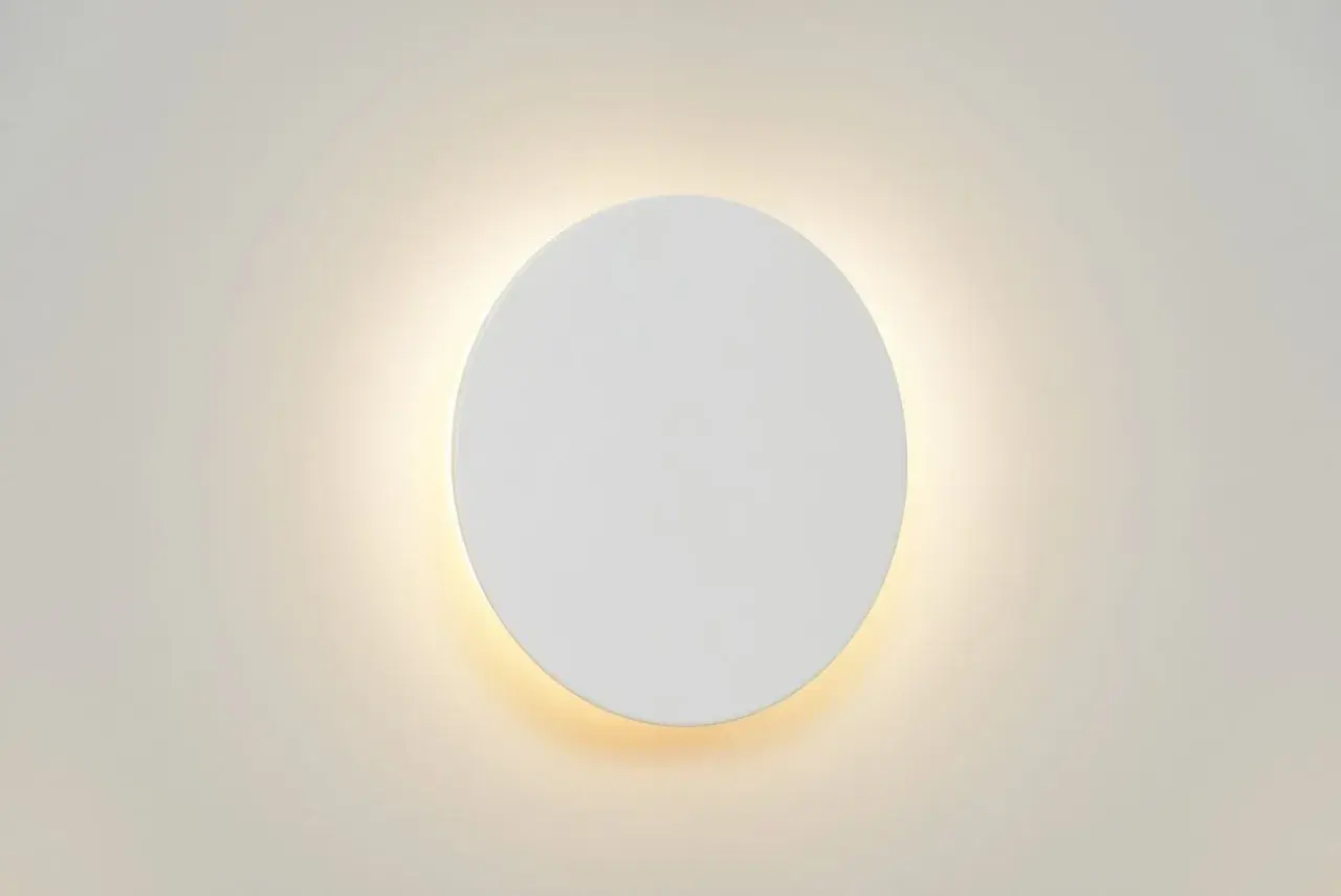 Un aplique redondo de pared blanco emite una luz cálida y difusa, creando un ambiente acogedor.