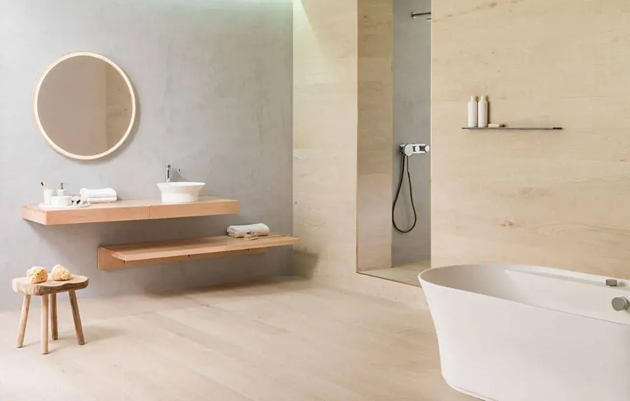 Baño moderno con lavabo flotante, bañera blanca y ducha. El suelo de madera clara contrasta con los azulejos de la pared.