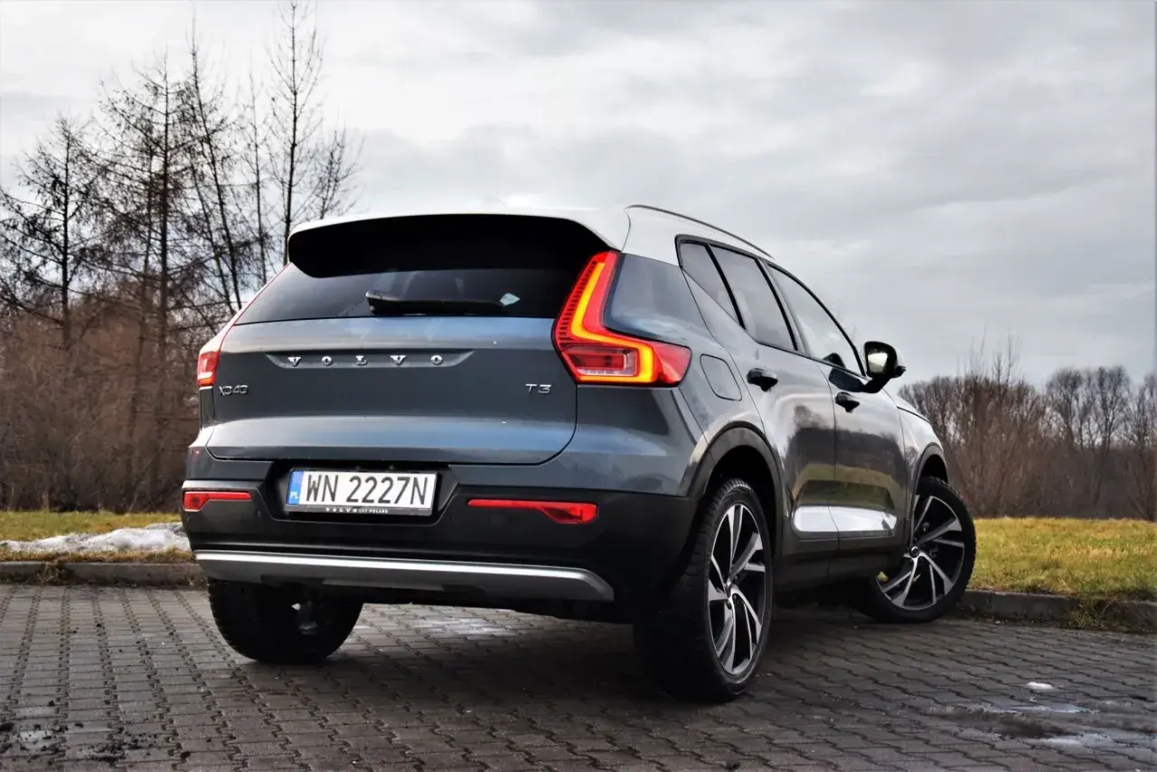 Tylny widok na ciemnoszary Volvo XC40 T3 z białym dachem, zaparkowany na brukowanej nawierzchni.