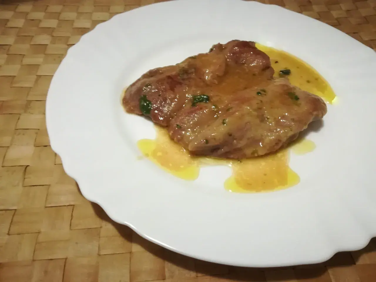 Due fettine di tacchino appetitose, immerse in una salsa dorata e profumata, servite su un piatto bianco.