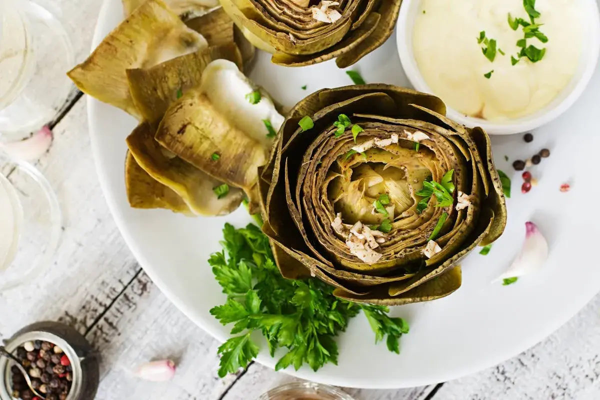 Deliciosas alcachofas al horno, tiernas y doradas, servidas con una cremosa salsa y perejil fresco. Un plato perfecto para disfrutar.