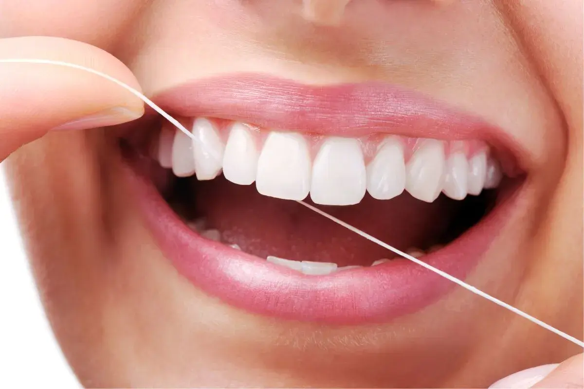 Dita che usano il filo interdentale per pulire i denti bianchi e perfetti. Un gesto quotidiano per un sorriso smagliante.