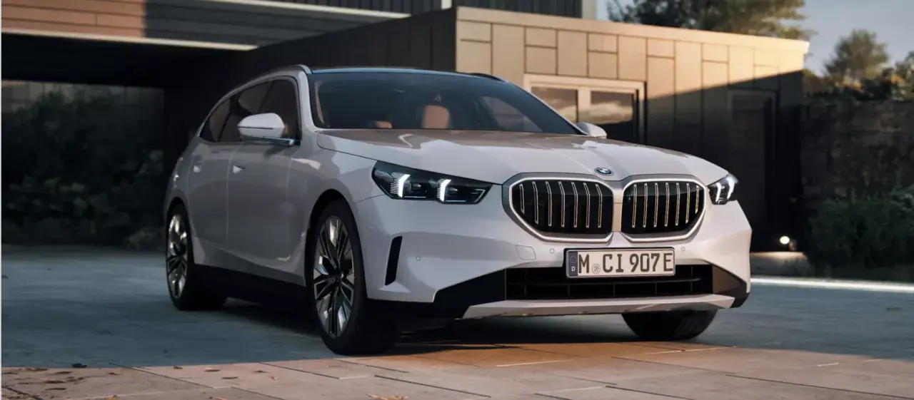 Białe BMW 550e z nowoczesnym grillem i światłami LED stoi przed minimalistycznym budynkiem.