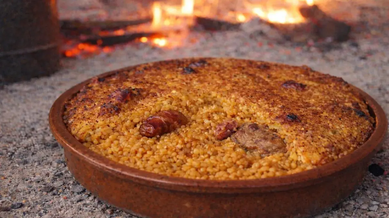 Arroz con costra recién hecho, con trozos de carne y salchicha, cocinándose a la leña.