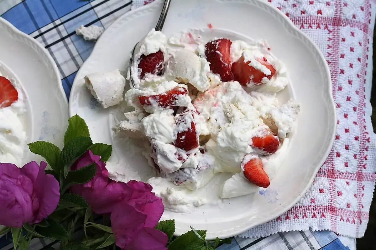 En härlig Eton Mess med färska jordgubbar och marängbitar, serverad på en vit tallrik med en vacker duk och rosor.