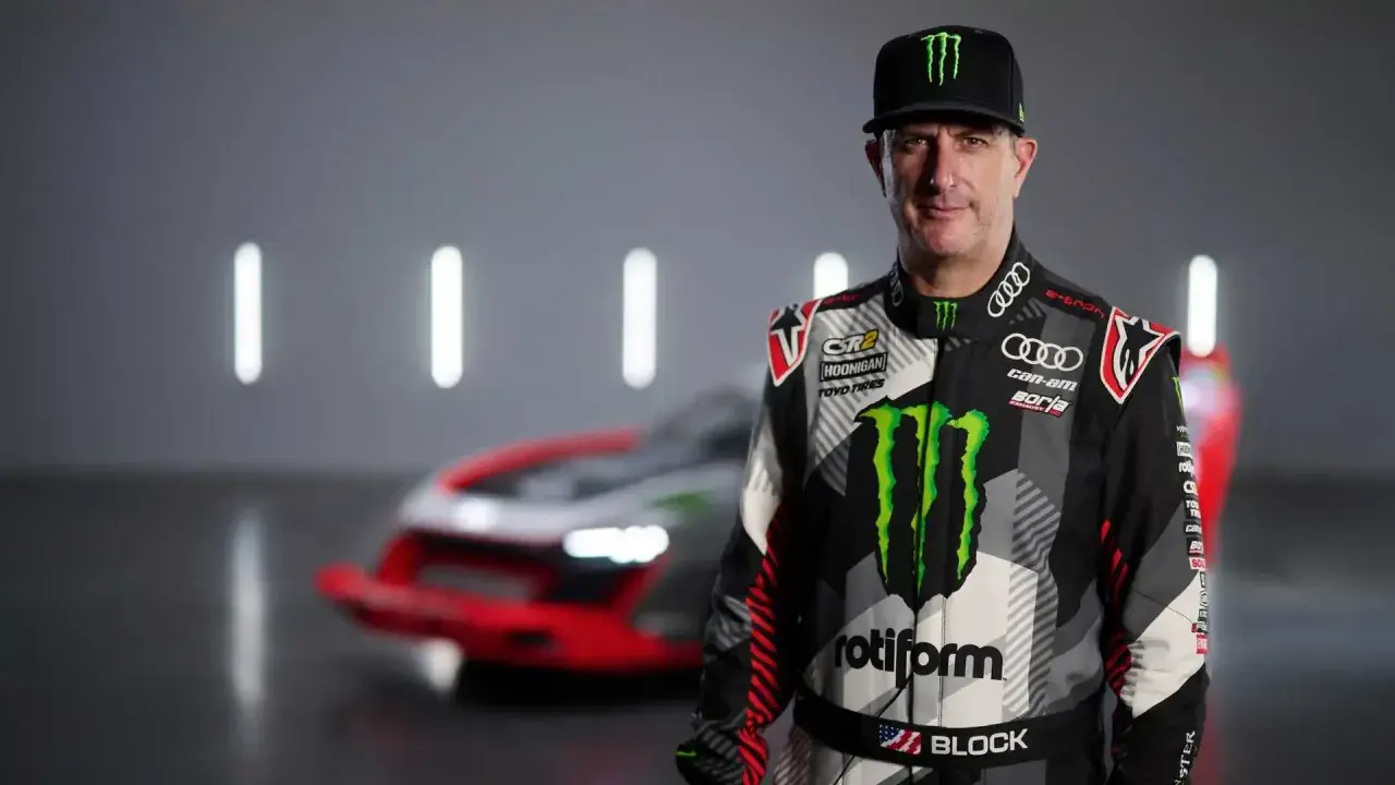 Ken Block, piloto de rally, posa con su traje de competición y un coche de Audi e-tron detrás.