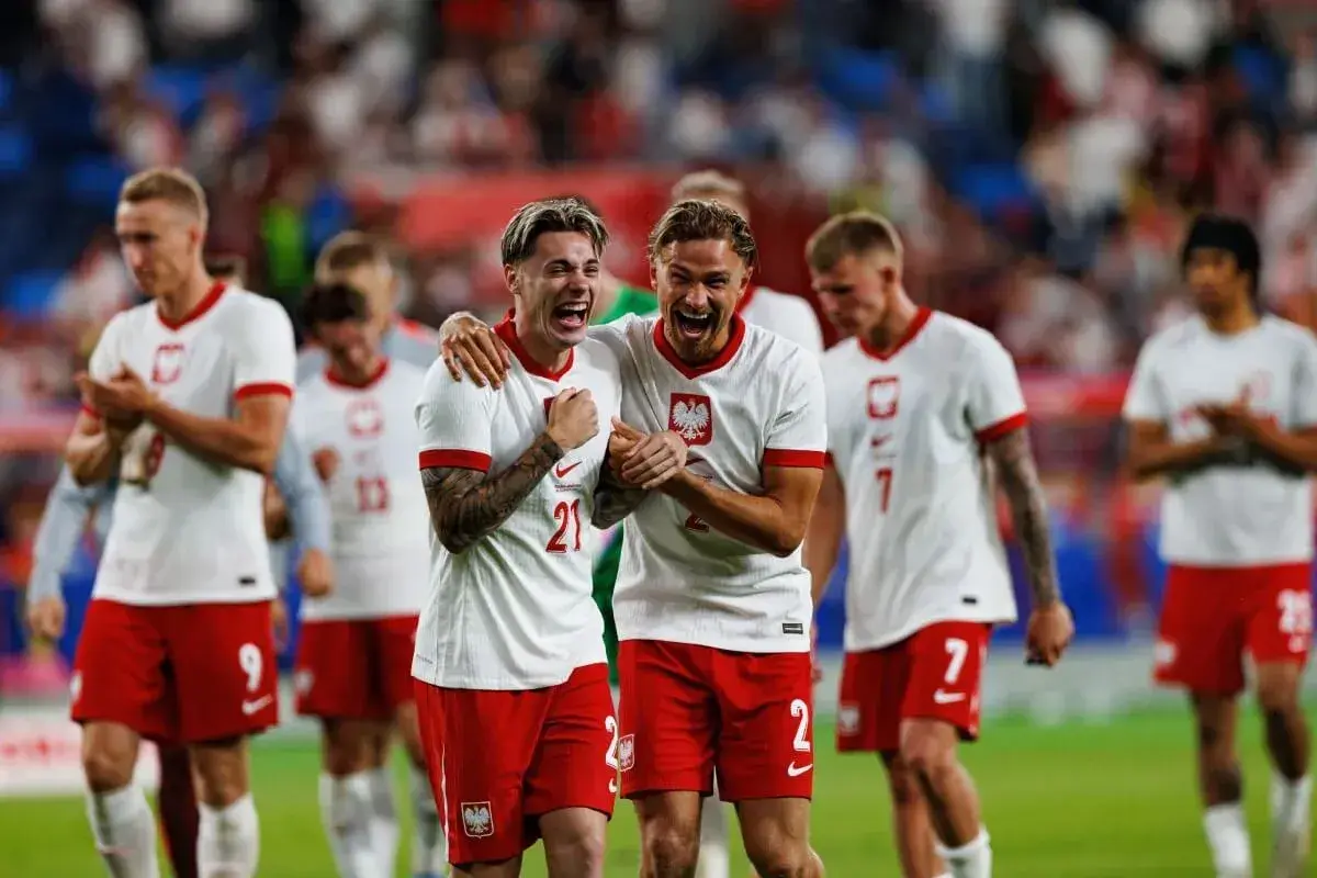 Piłkarze Polski świętują zwycięstwo nad Finlandią. Dwóch zawodników w białych koszulkach z orłem na piersiach, z szeroko otwartymi ustami, cieszy się z sukcesu.