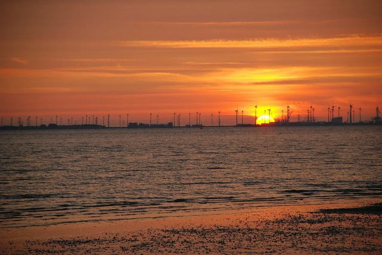 Sonnenuntergang am Emden Strand mit Windrädern und glitzerndem Wasser.