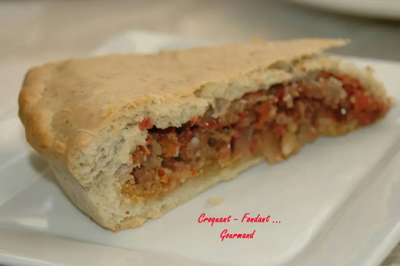 Une part d'impanata siciliana, une tourte sicilienne garnie d'une farce savoureuse, sur une assiette blanche.