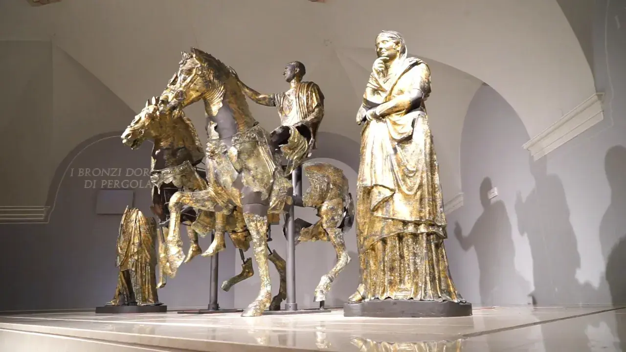 Bronzi dorati di Pergola: un cavaliere su un cavallo, una figura femminile e altre statue antiche.