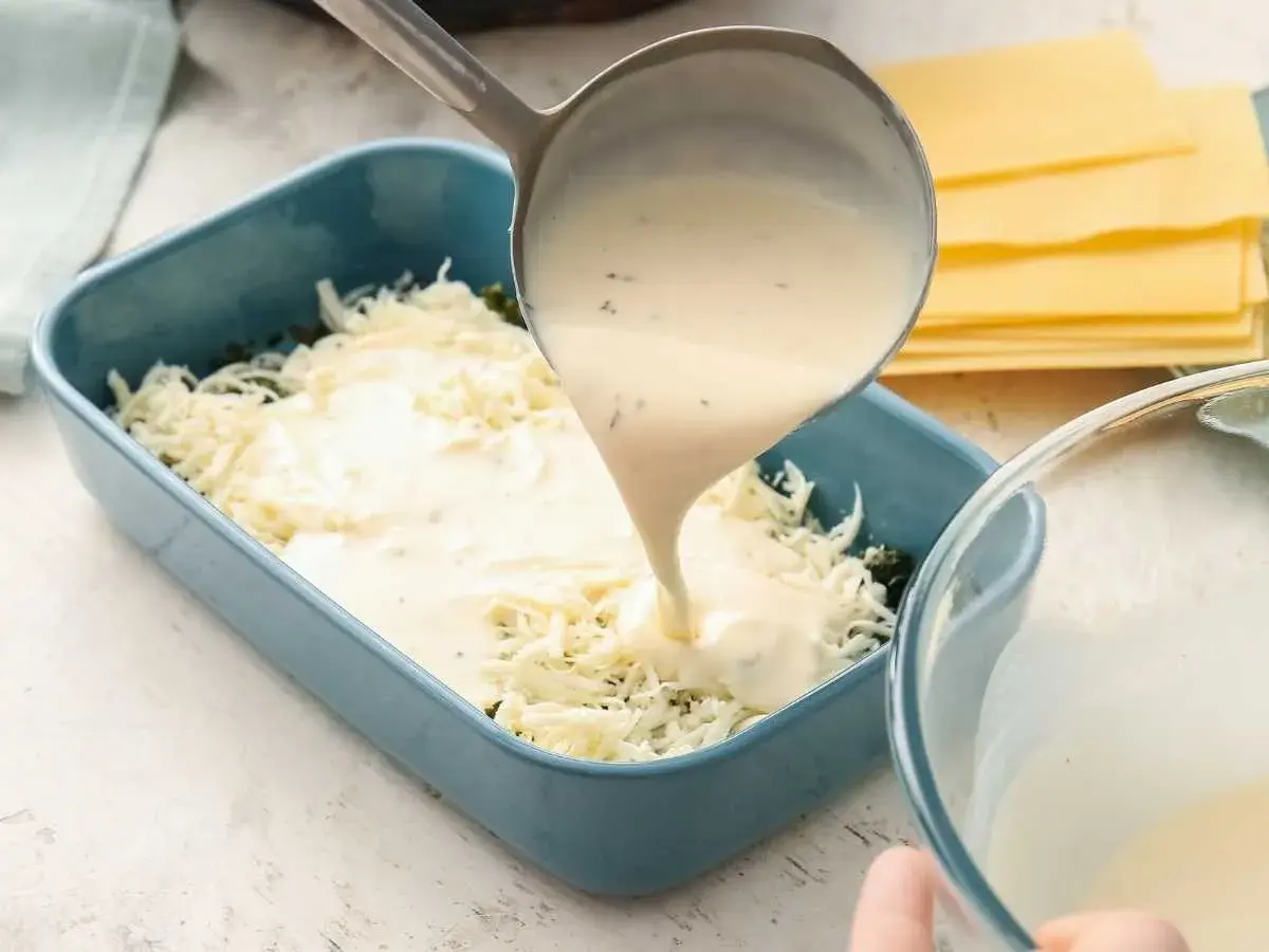Se vierte bechamel para lasaña sobre queso rallado en un molde azul.