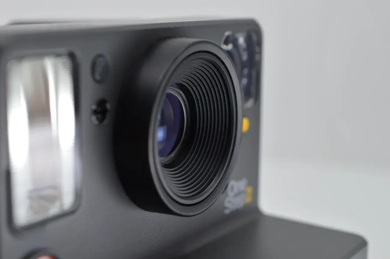 Zbliżenie na obiektyw aparatu Polaroid One Step 2. Widoczny błysk flesza i detale obudowy, sugerujące eksperymenty z bracketingiem ostrości.