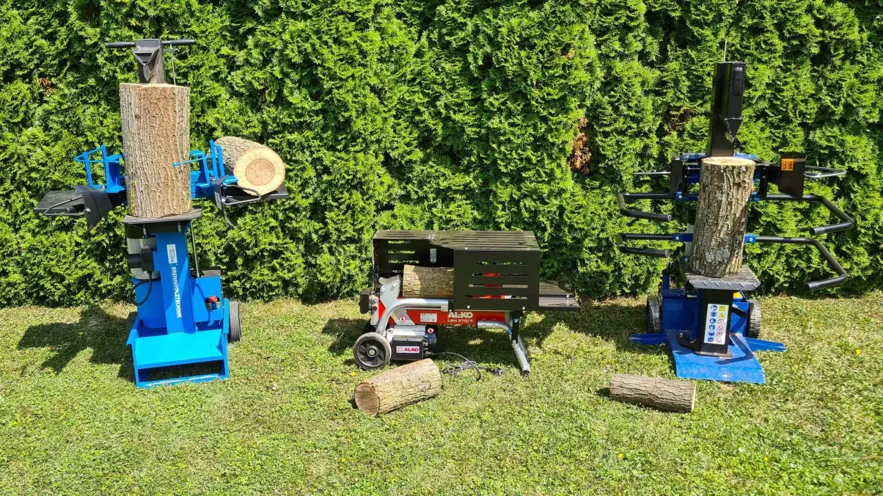 Zwei Holzspalter, einer davon mit Einhandbedienung, stehen im Gras vor einer grünen Hecke.
