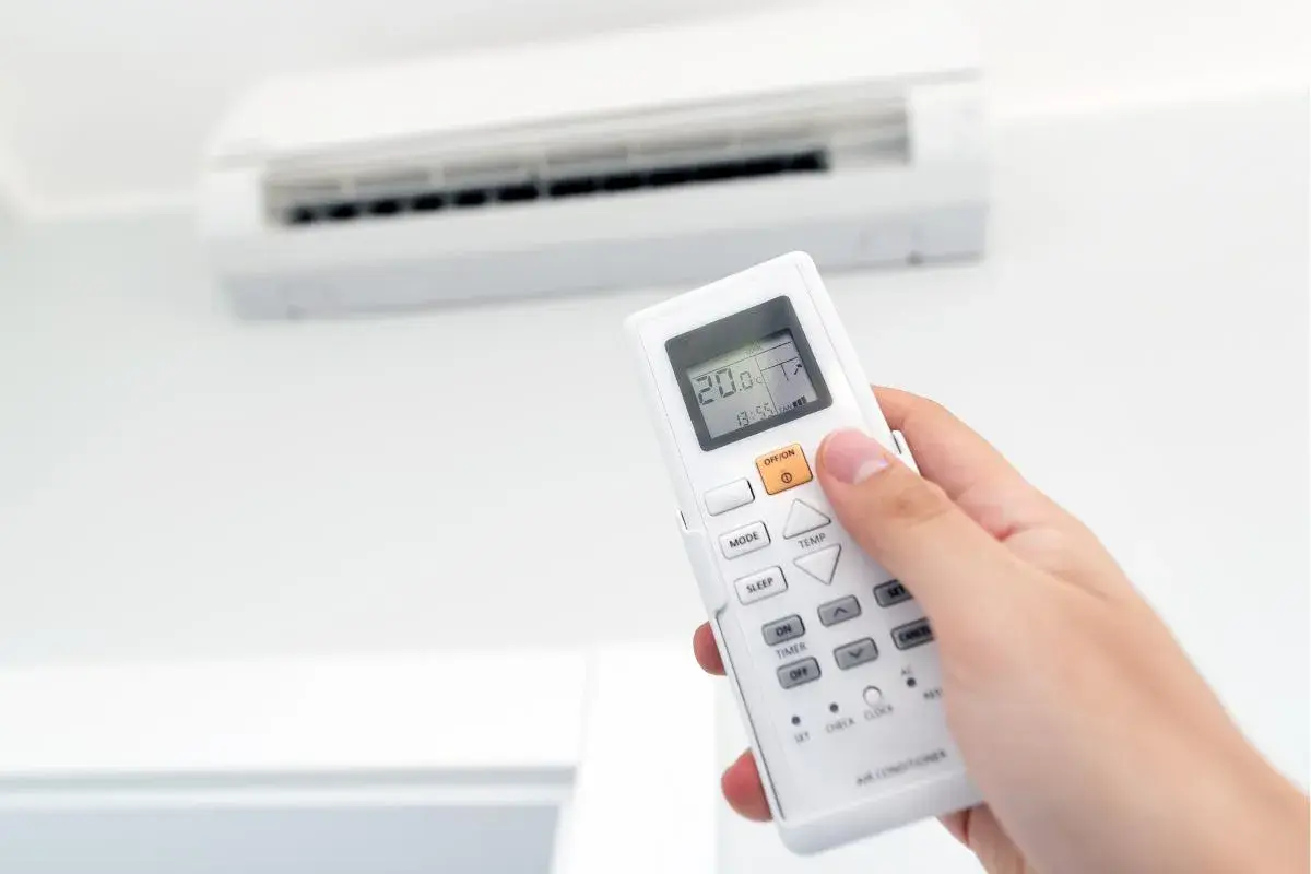 Mano sujetando un control remoto de aire acondicionado, ajustando la temperatura para combatir el calor o el frío.