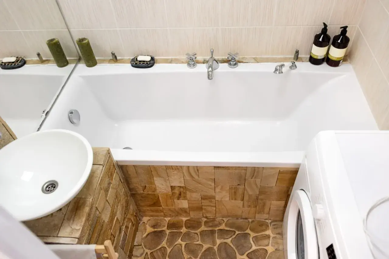 Badezimmer mit Waschbecken, Badewanne verkleiden mit Naturstein und Waschmaschine.
