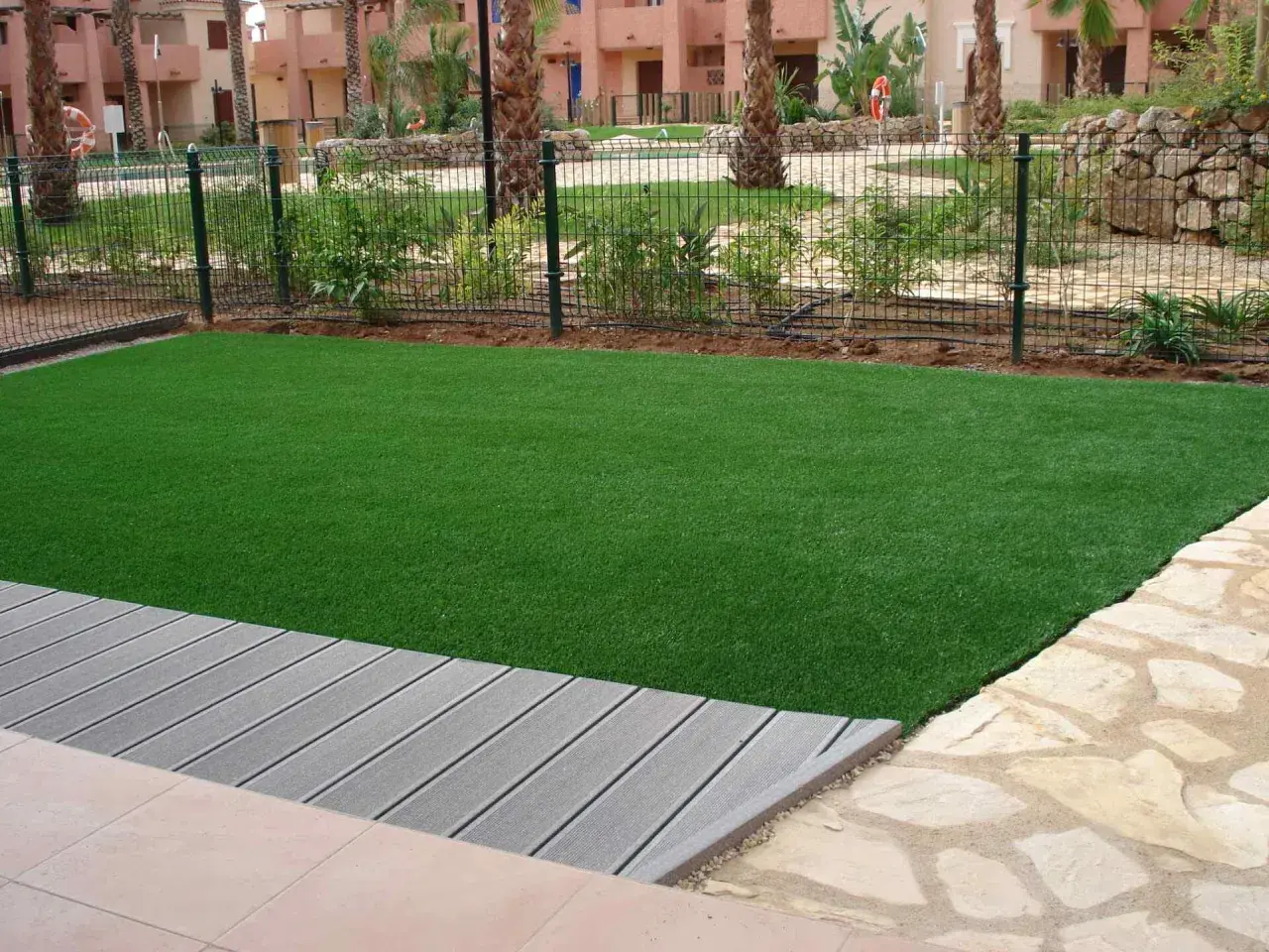 Césped artificial verde vibrante junto a una terraza de madera gris. El césped artificial puede generar electricidad estática.