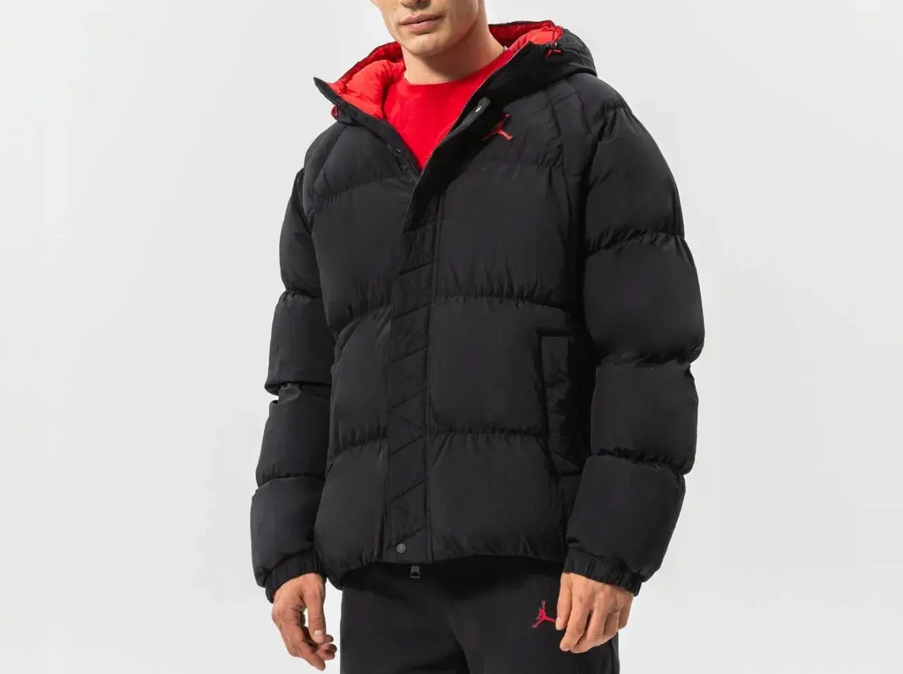 Mężczyzna w czarnej, puchowej kurtce Jordan Essentials z czerwonym wykończeniem i logo Jumpman.