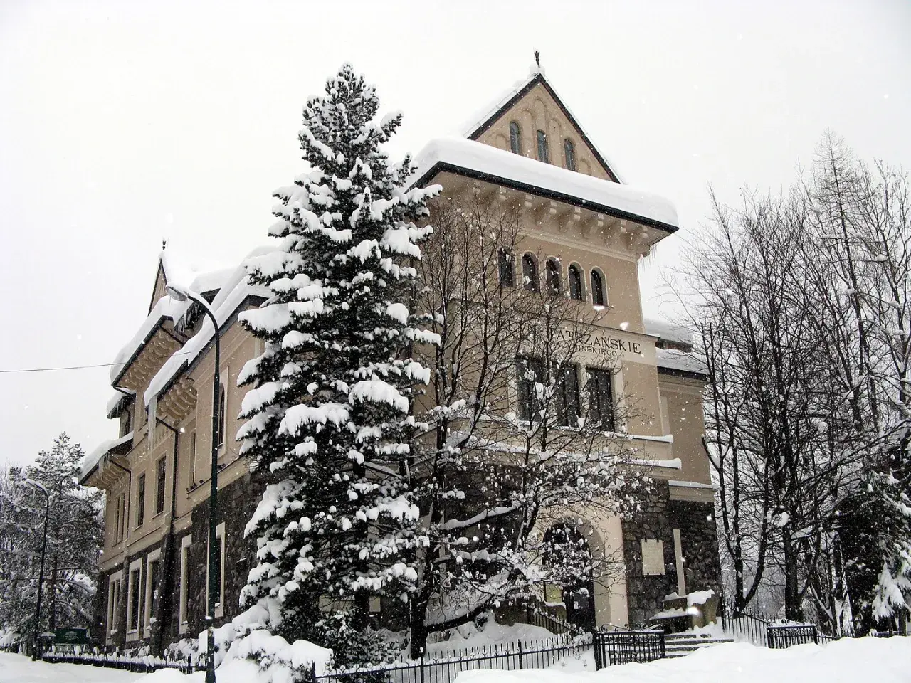 Zimowy dzień w muzeum Tatrzańskiego Parku Narodowego. Śnieg otula drzewa i budynek, tworząc bajkową scenerię.