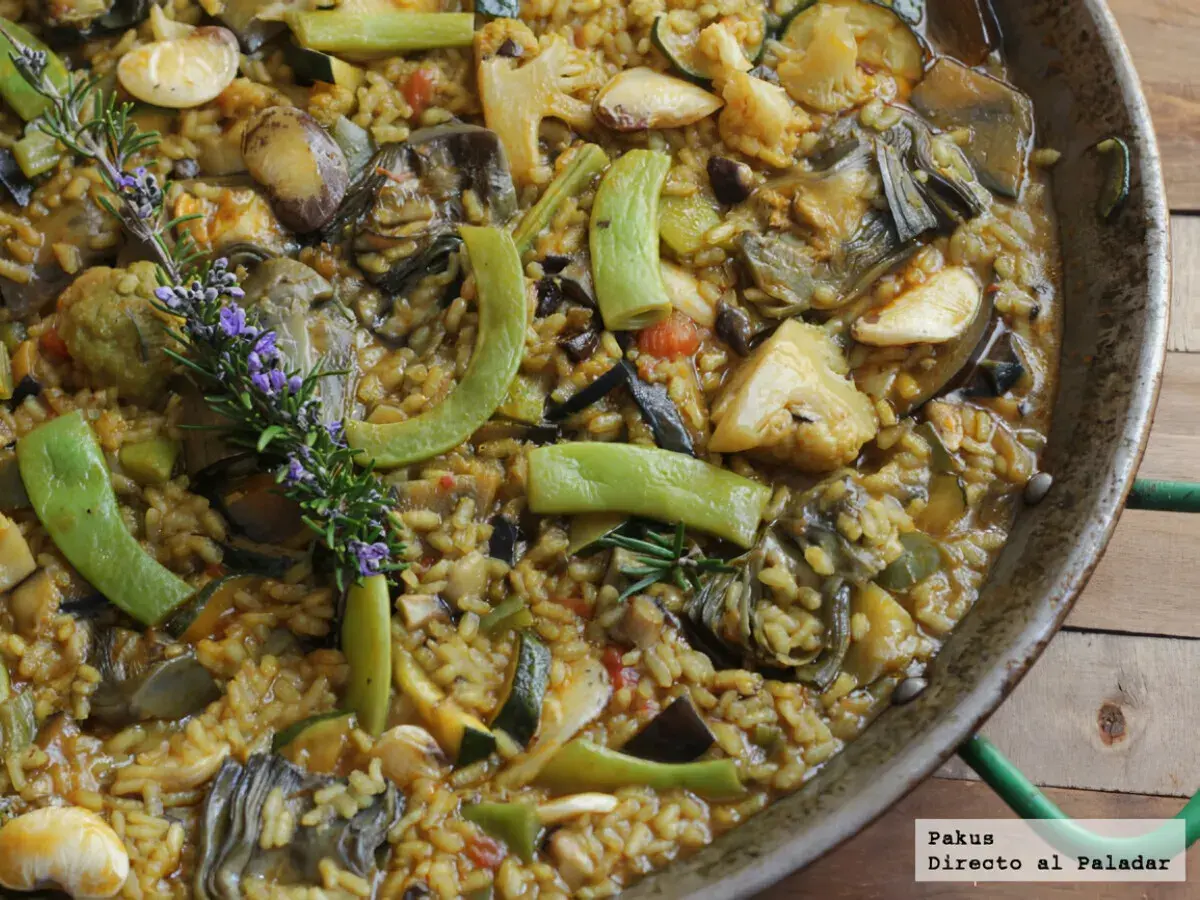 Paella de verduras vibrante, con alcachofas, calabacín, pimientos y romero fresco. Un festín para la vista y el paladar.