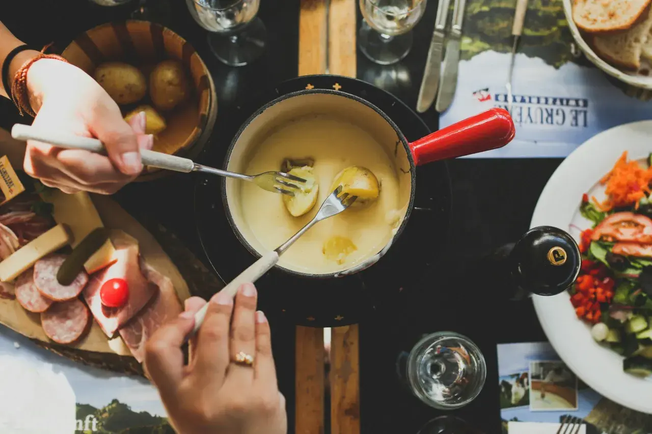 Des mains trempent des pommes de terre dans une fondue savoyarde, un délice de fromages fondus suisses.