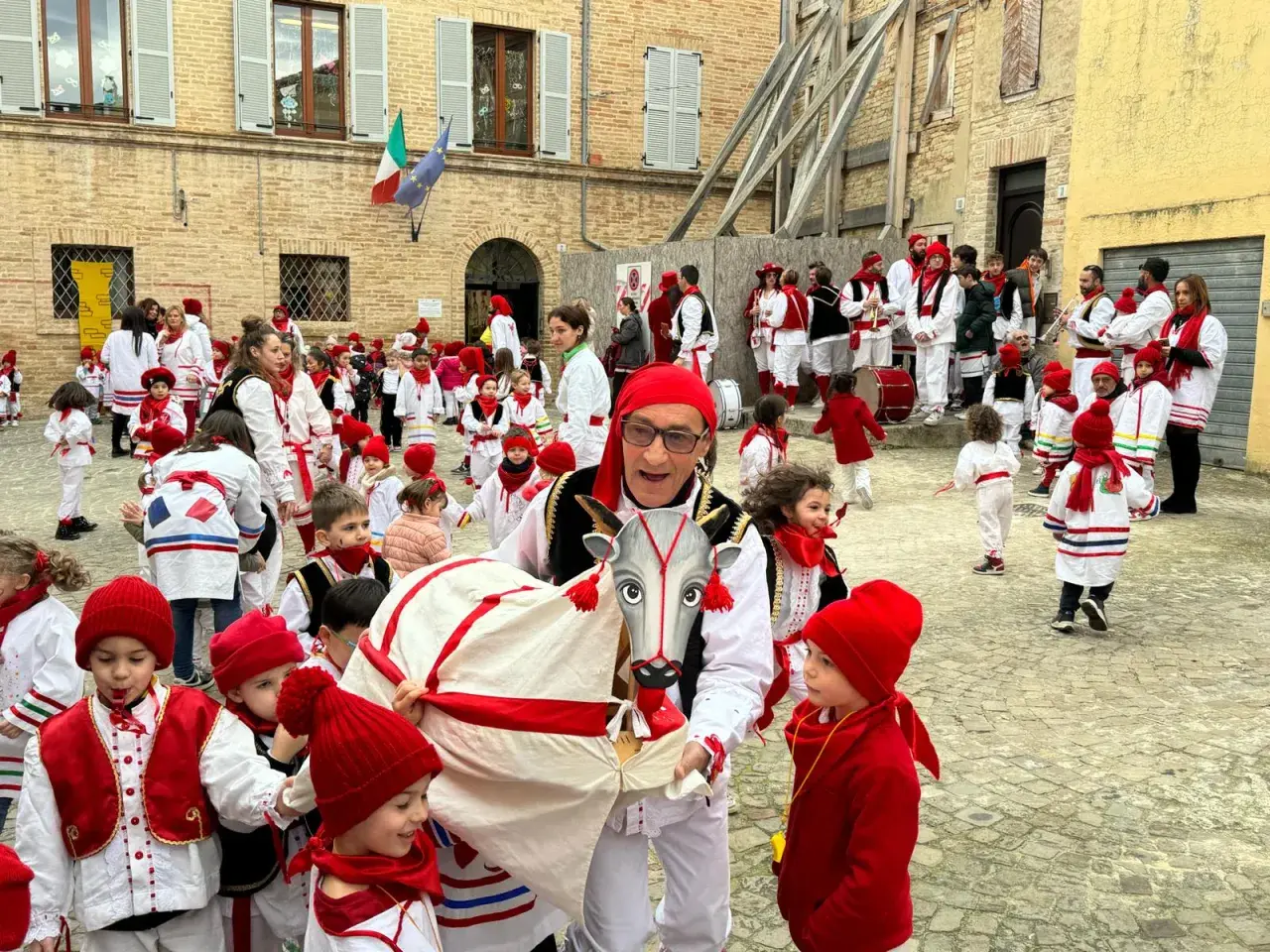 Un uomo con un costume da toro guida una sfilata di bambini vestiti di rosso e bianco per il carnevale nelle Marche.