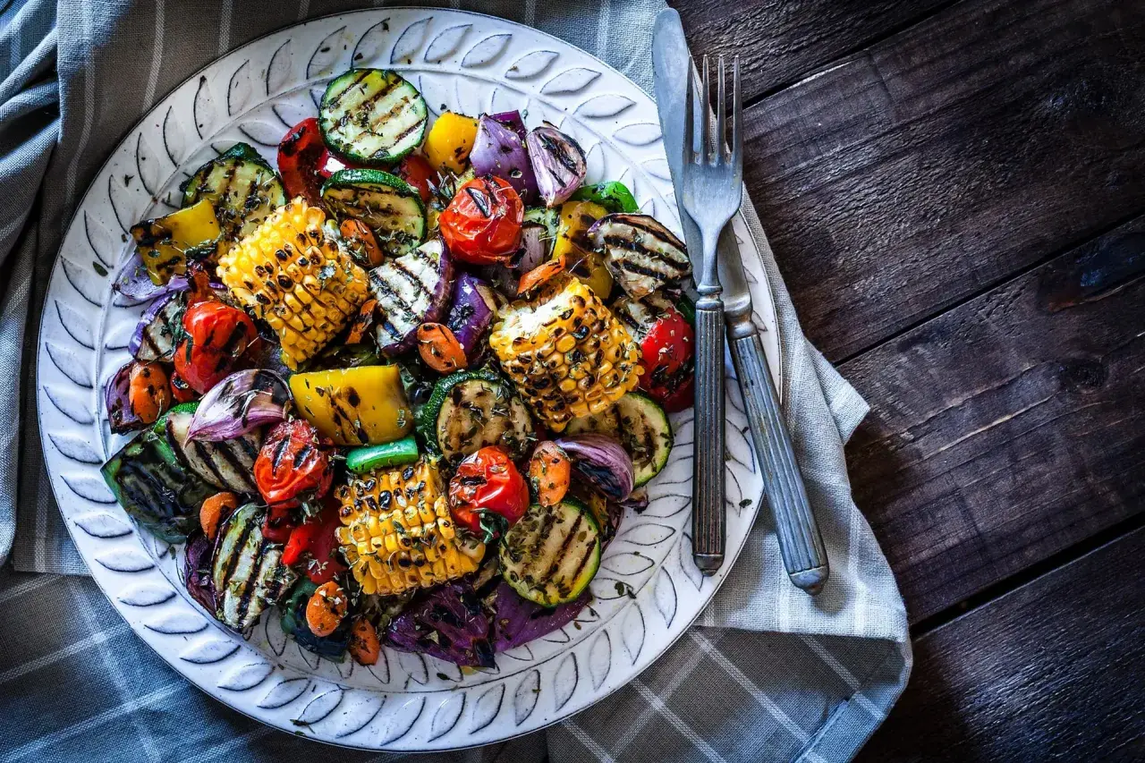 Assortiment coloré de légumes plancha : courgettes, maïs, poivrons, tomates cerises et oignons rouges grillés, assaisonnés d'herbes.