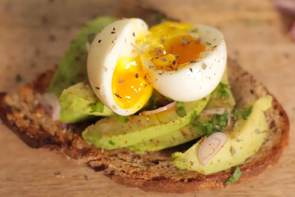 Tartine oeuf et avocat, un délice crémeux avec un jaune coulant, garnie d'herbes fraîches et d'épices sur du pain grillé.